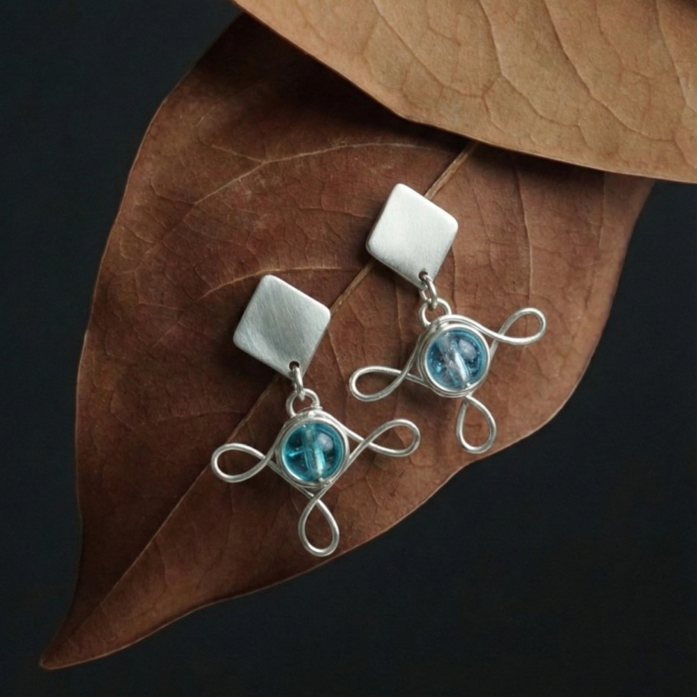 Blue and Silver Earrings on Brown Leaves. Dark Background