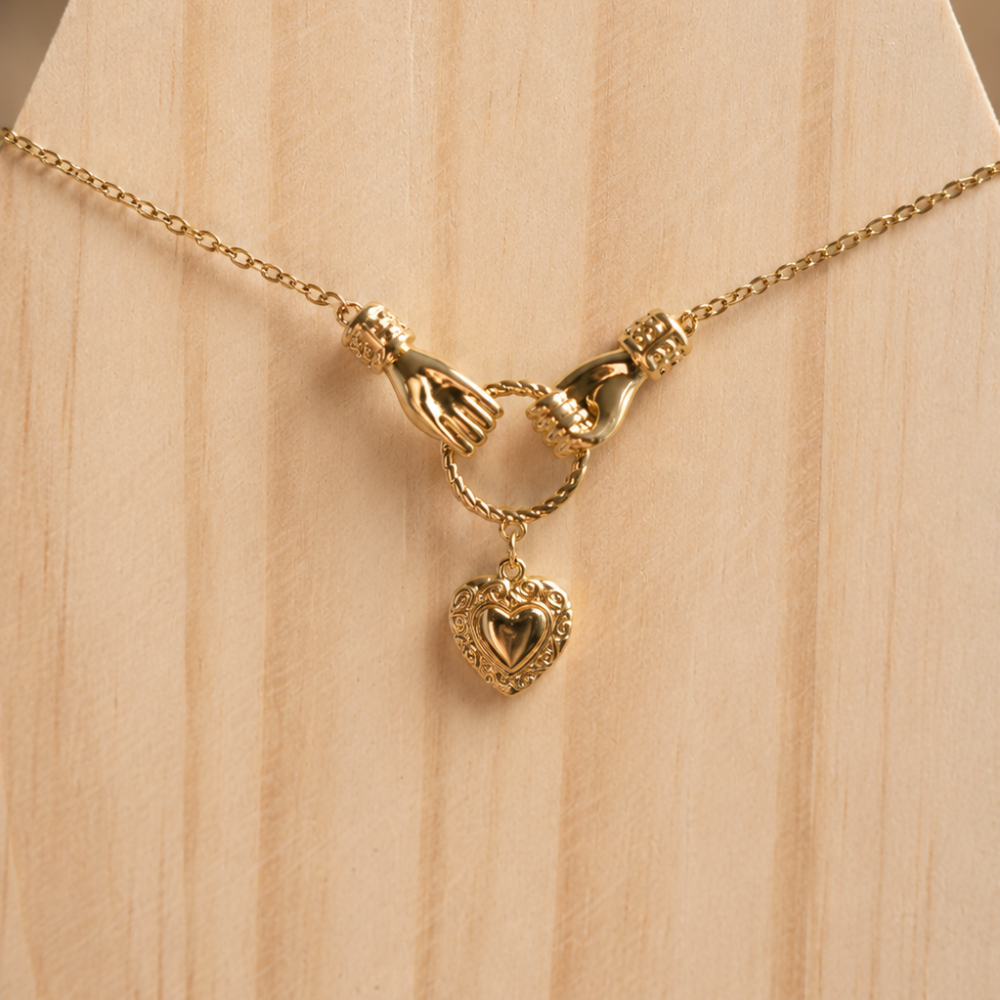 A romantic gold necklace with two delicate hands holding a heart pendant. Made from 304 stainless steel with 18k gold PVD coating and zircon detail.