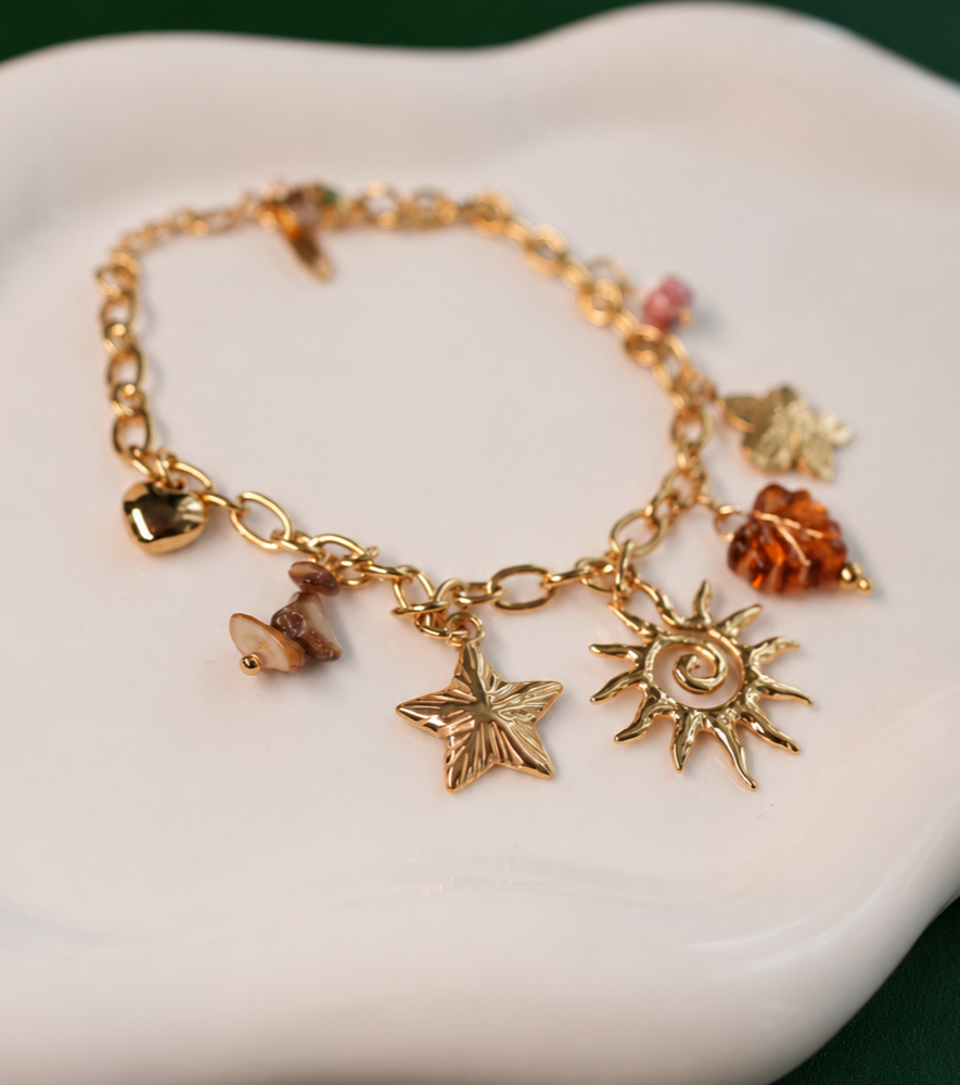 A gold charm bracelet with sun, flower, heart, leaf, and warm-toned bead details. A playful nature-inspired piece from the Neréa Anthi Curated Collection.