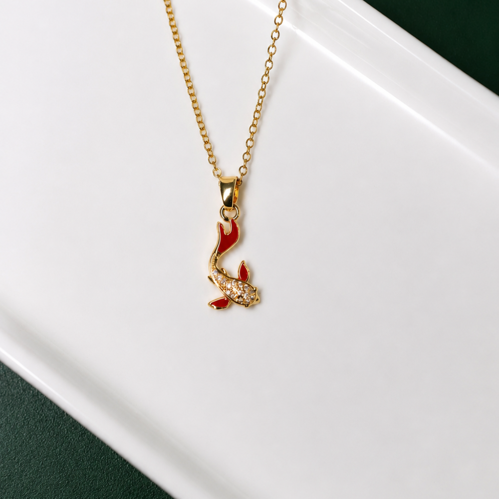 A gold koi fish necklace with rich red accents and sparkling zircon details. A symbolic statement piece from the Neréa Anthi Curated Collection.