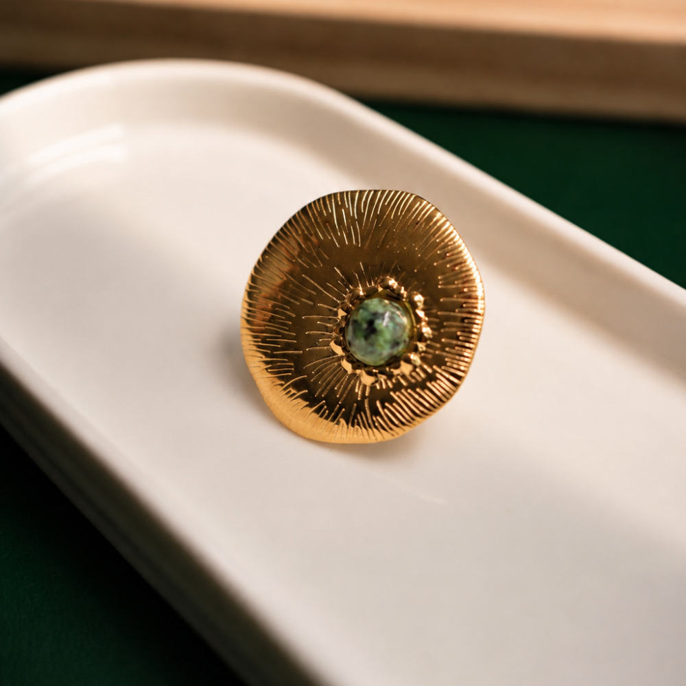 An adjustable 14k gold-plated stainless-steel ring with a textured circular design and domed green stone. Part of the Neréa Anthi Curated Collection.