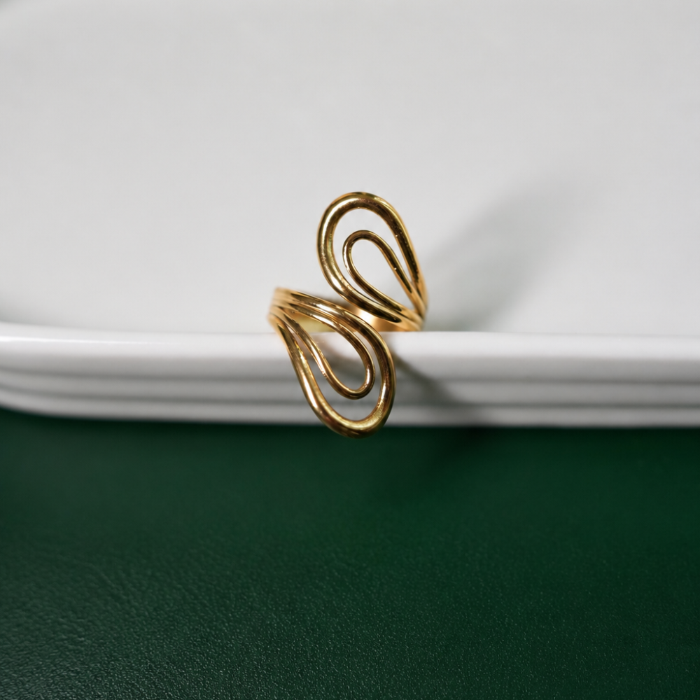 An adjustable sculptural gold ring with flowing double-loop details, made from 18k gold PVD-coated stainless steel. Part of the Curated Collection.