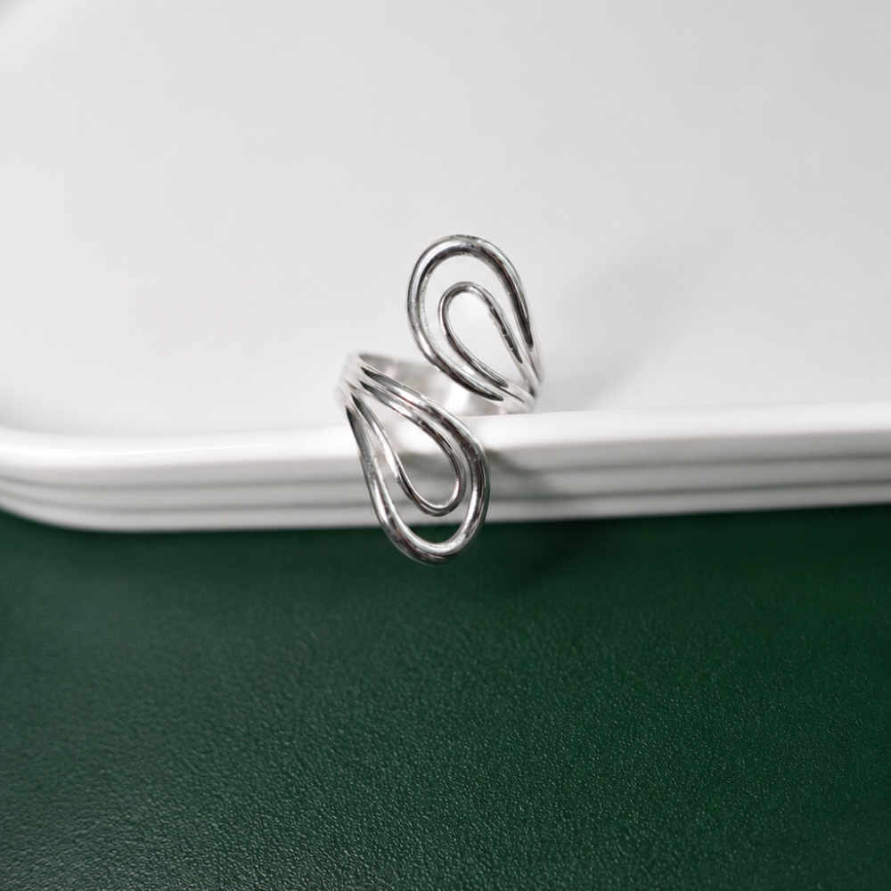 An adjustable sculptural silver ring with flowing double-loop details, made from PVD-coated stainless steel. Part of the Curated Collection.
