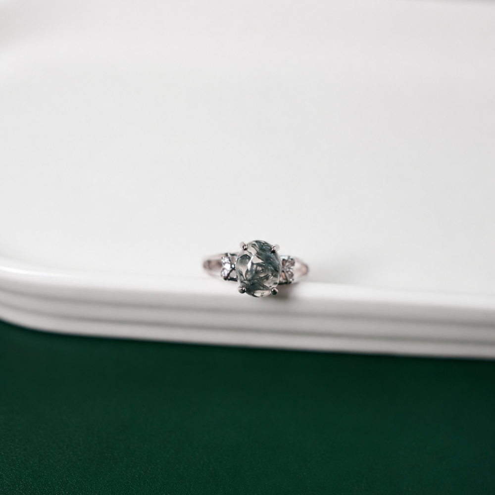 A delicate silver-tone open ring with a natural moss agate centre stone and subtle clear details. A refined piece from the Neréa Anthi Curated Collection.